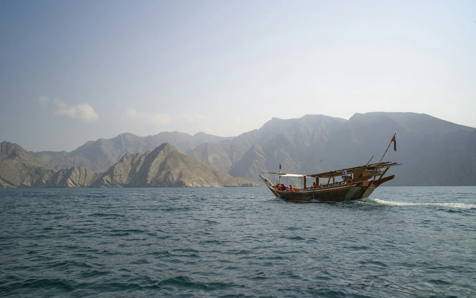 Un tradizionale dhow in legno su acque turchesi sotto le scogliere calcaree dei fiordi di Musandam